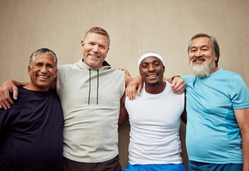Four men of different ages stand side by side in casual t-shirts, facing the camera.