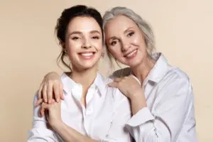 A younger and an older woman in white shirts standing arm in arm and smiling