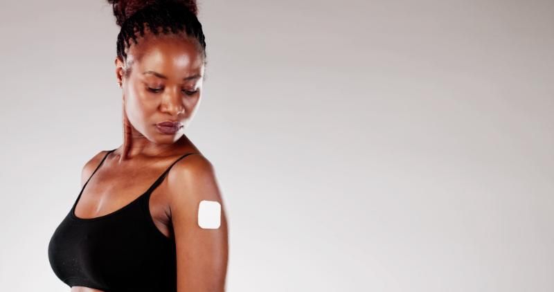 A woman in a black top with a small square adhesive patch applied to her upper arm.