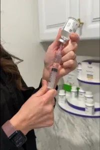 Hands drawing liquid from a vial into a syringe in front of a supplement display