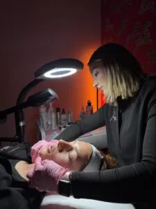 Treatment room with a lit ring lamp where a practitioner works on a reclining client's face