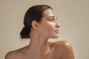 Studio profile portrait of a woman with her hair tied back against a tan background
