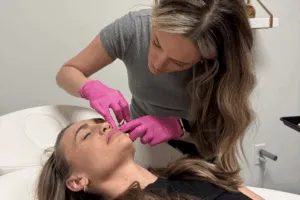 Clinician wearing gloves holding a syringe to the lip of a client lying on a treatment bed