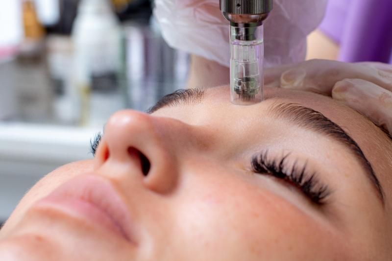 Close view of a gloved hand holding a pen-shaped device against the forehead of a woman lying with her eyes closed.